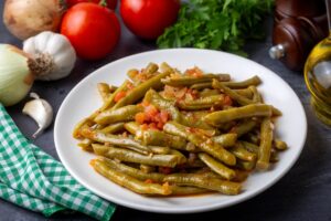 Crohn's friendly Greek green beans with tomatoes, garlic, and oregano on a white plate