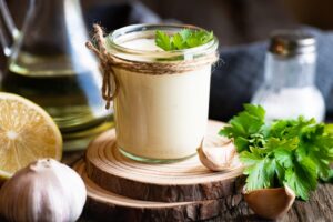 Jar of homemade Paleo aioli with garlic, lemon, parsley, and olive oil on a rustic wooden board
