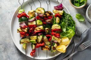 Grilled Paleo vegetable skewers with zucchini, peppers, onions, and tomatoes on a plate with lemon wedges