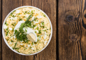 Bowl of Paleo egg salad topped with chopped herbs and half a boiled egg on a wooden table
