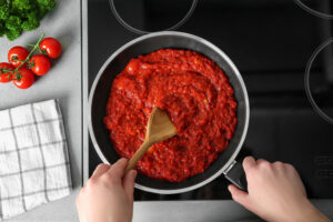 Homemade marinara sauce simmering in a pan, stirred with a wooden spoon.