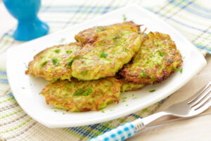 Golden-brown zucchini fritters garnished with fresh herbs, served on a white plate with a fork.