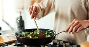 Person cooking Paleo vegetables in a skillet with spinach, onion, and red bell pepper.