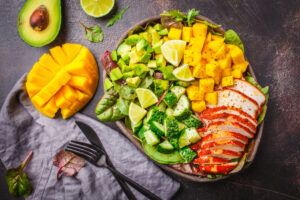Paleo chicken, mango, avocado, and cucumber salad with lime wedges.
