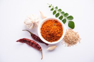 Bowl of homemade Paleo chili powder with garlic, dried red chilies, sesame seeds, and curry leaves on a white background
