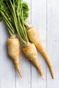 Fresh raw parsnips with green tops on a white wooden surface