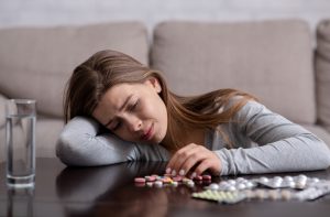 Sad young woman leaning on a table with various pills in front of her, symbolizing struggles with antidepressant use.
