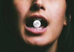 Close-up of a woman holding a pill labeled ‘happy’ in her mouth, symbolizing antidepressant use