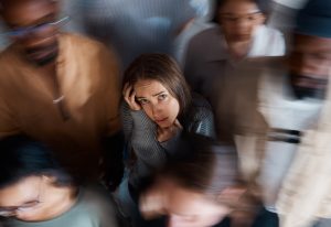 An anxious woman standing in a crowd with motion blur around her, symbolizing overwhelm and anxiety.