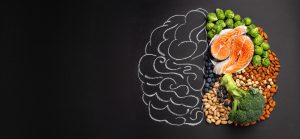 Assorted brain-healthy foods including salmon, nuts, broccoli, and blueberries arranged in the shape of a brain, symbolizing how B vitamins and nutrition support cognitive health.